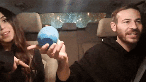 a man and a woman are in a car and the man is holding a blue object
