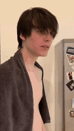 a shirtless man with a towel around his neck is standing in front of a refrigerator that has a merry christmas sign on it