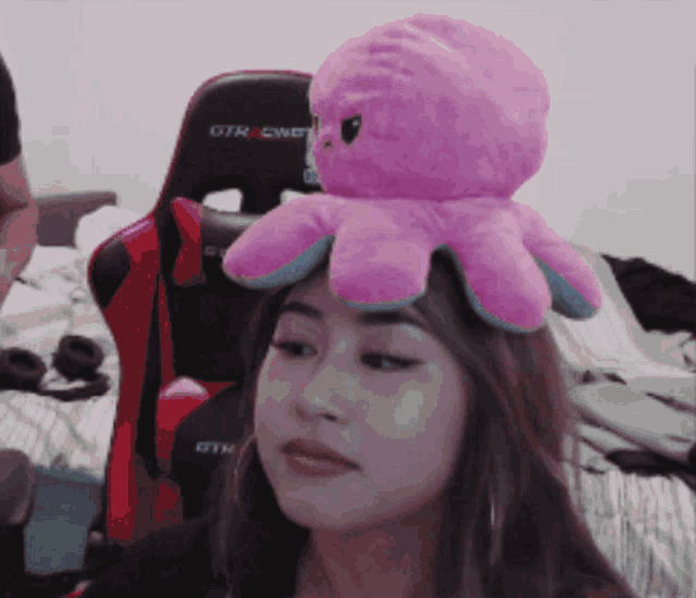 a woman with a stuffed octopus on her head in front of a gtracing chair