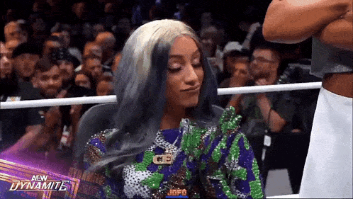 a woman with gray hair is sitting in a chair in a wrestling ring in front of a crowd .