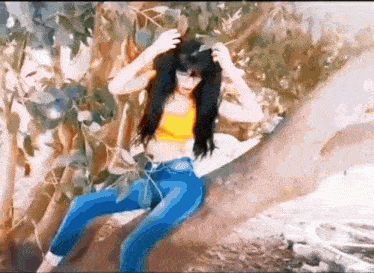 a woman in a yellow top and blue jeans is sitting on a tree .
