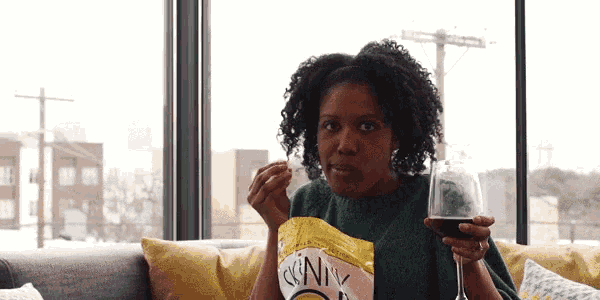 a woman sitting on a couch with a bag of crunchy potato chips and a glass of wine