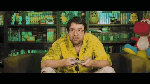 a man in a yellow shirt and glasses is playing a video game with a controller .
