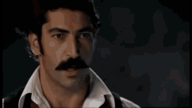 a man with a mustache is looking at a piece of paper with his eyes closed .