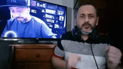 a man wearing headphones and a ny hat stands in front of a television