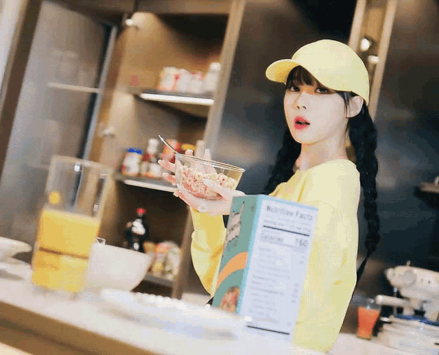 a girl in a yellow hat holds a bowl of cereal and a box of nutrition facts