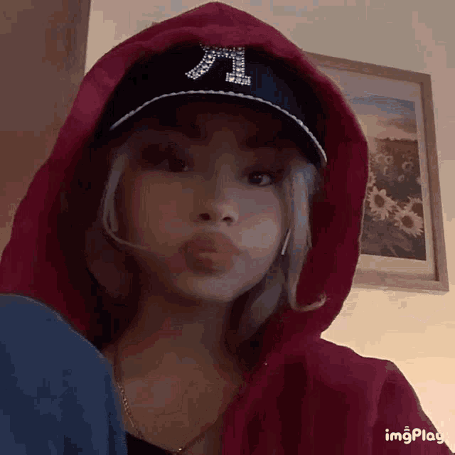 a girl wearing a red hoodie and a baseball cap with the letter t on it