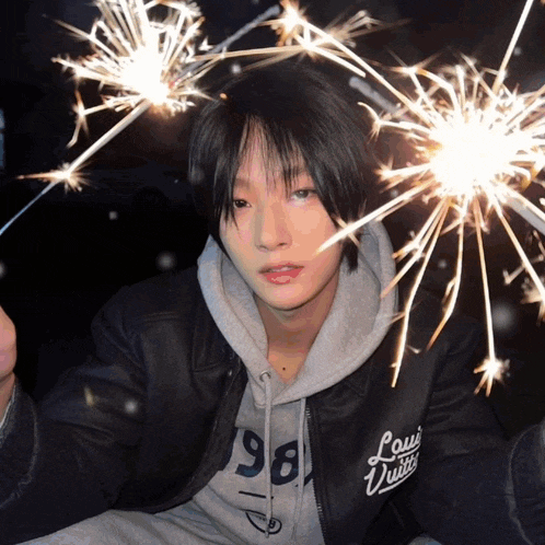 a person wearing a louis vuitton jacket holds sparklers in front of their face