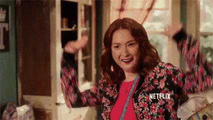a woman in a floral jacket is standing in a room with her arms outstretched and smiling .