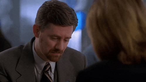 a man in a suit and tie talks to a woman in a black jacket