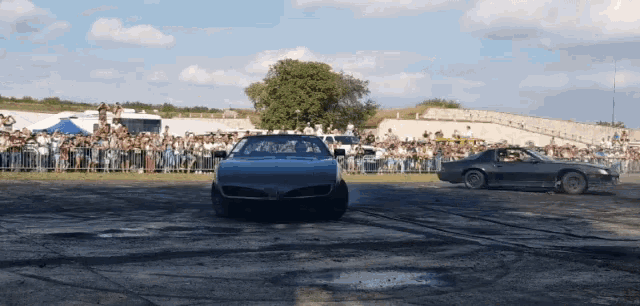 two cars are drifting in front of a crowd watching