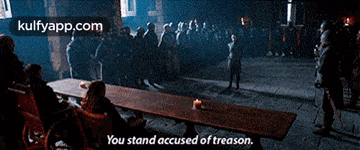 a group of people sitting around a long wooden table with the words you stand accused of treason ..