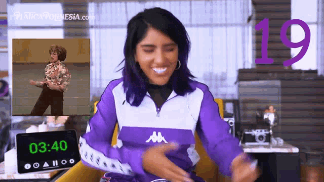 a woman in a purple kappa jacket is sitting in front of a clock that says 03:40