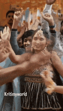 a woman is dancing in front of a crowd with her hands in the air and the words kritimyworld on the bottom