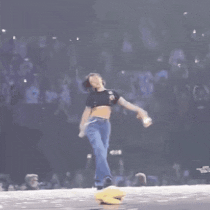 a woman in a black crop top and blue jeans walking on a stage