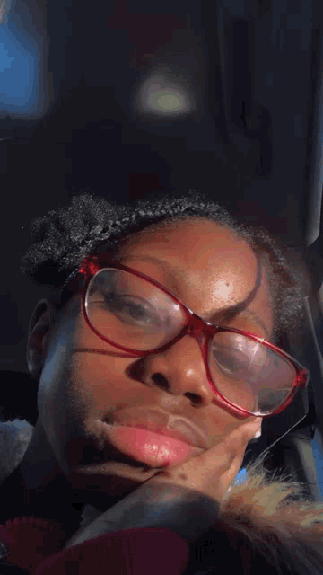 a woman wearing red glasses looks at the camera with her hand on her chin