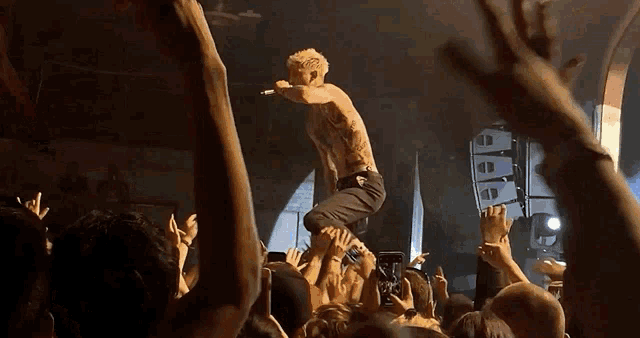 a shirtless man is singing into a microphone in front of a crowd that is raising their hands