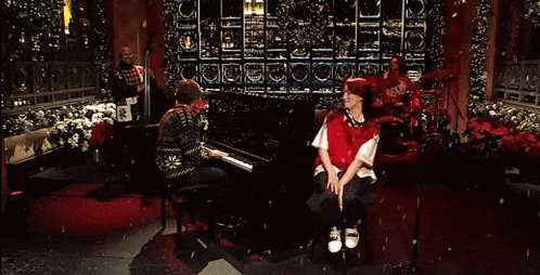 a woman playing a piano and a girl singing in front of a christmas tree