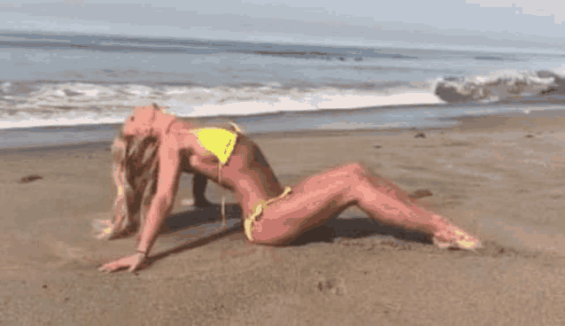 a woman in a yellow bikini is laying on a sandy beach .