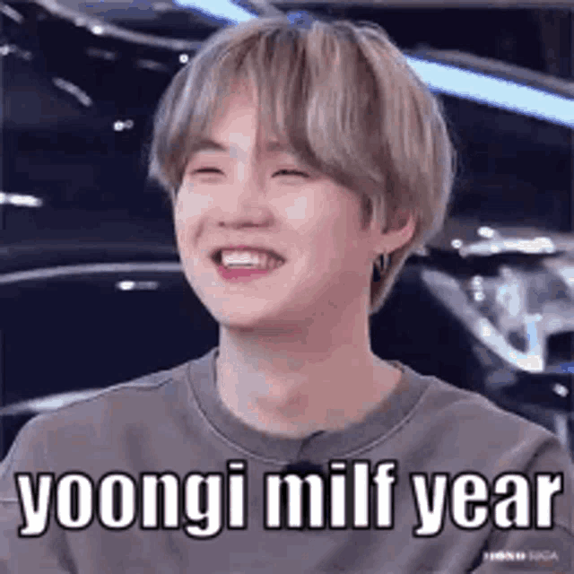a young man is smiling and laughing with the words `` yoongi milf year '' written on his face .