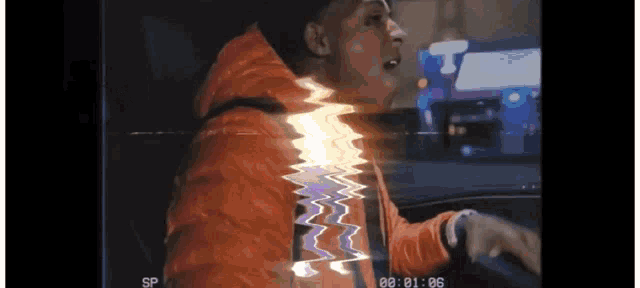 a man in an orange jacket is driving a car with a glitch effect on the screen .