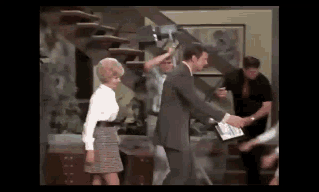a man in a suit and a woman in a skirt are shaking hands in a room .