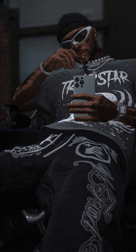 a man wearing sunglasses and a shirt that says star takes a selfie with his phone