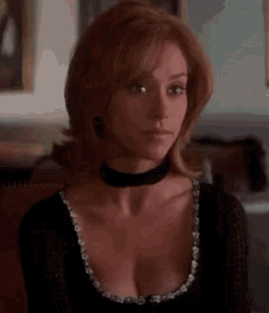 a woman wearing a choker and a black top is sitting in a room .