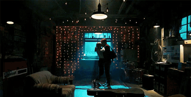 a man and woman are hugging in a dark room with a guitar case in front of them