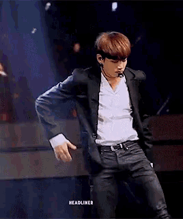 a man in a suit and white shirt is dancing on a stage with the word headliner in the corner
