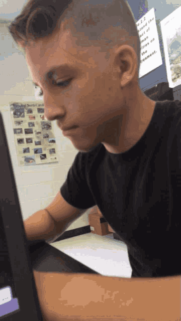 a boy in a black shirt is looking at a laptop computer