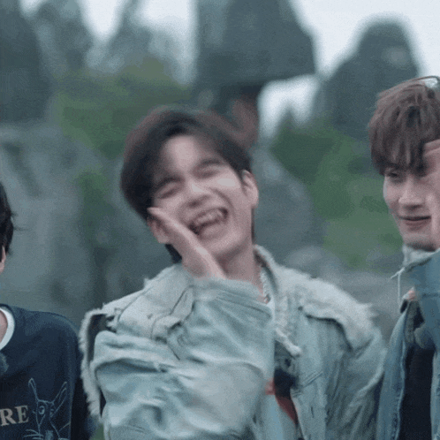 a man in a denim jacket is laughing while standing next to another man .