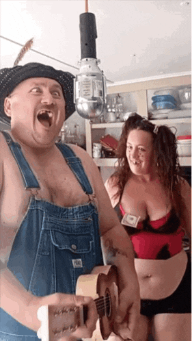 a man in overalls is playing a guitar next to a woman in a red bra