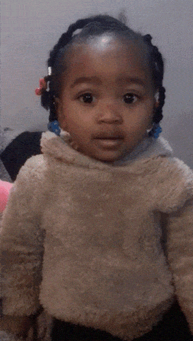 a little girl with braids in her hair is wearing a furry jacket