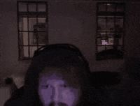 a man with a beard is wearing headphones in a dark room with a window in the background .