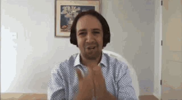 a man wearing headphones is clapping his hands while sitting at a desk .