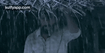 a man with a beard is standing under a straw roof in the rain .