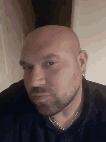a bald man with a beard is wearing a black shirt and a silver chain around his neck