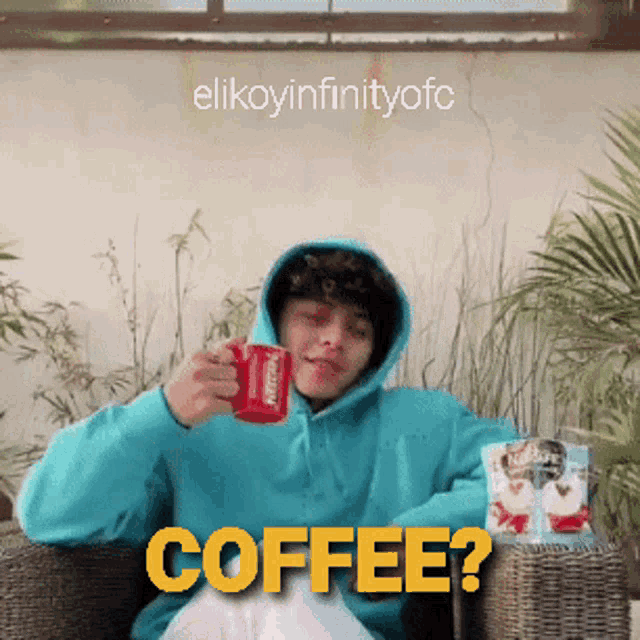 a man in a blue hoodie is sitting in a chair holding a red cup of nescafe coffee