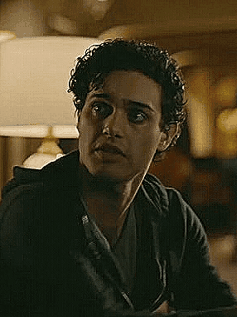 a young man with curly hair is sitting at a table in a dark room .