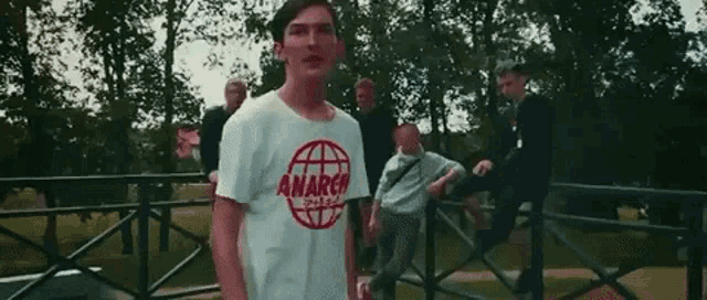 a man wearing a white t-shirt that says anarchy is standing in front of a group of people .
