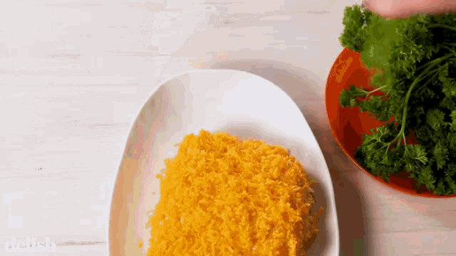 a plate of shredded cheese next to a bowl of parsley with the word delish on the bottom