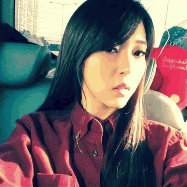 a woman in a red shirt is taking a selfie in a car with a red bag that says ' agatha '