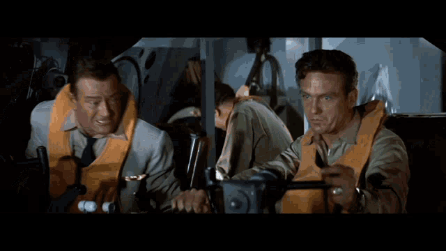 a man wearing a life vest talks to another man in a suit