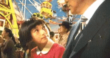 a little girl looking up at a man in a suit at a carnival