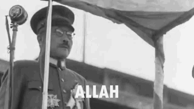 a man in a military uniform stands in front of a microphone and the word allah is visible