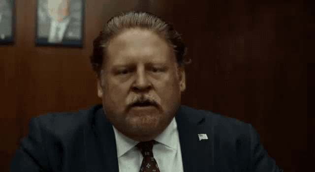 a man in a suit and tie is smoking a cigarette in a room .