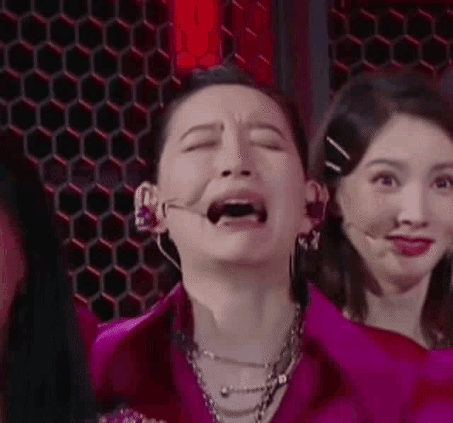 a woman is making a funny face with her mouth open while standing next to another woman .