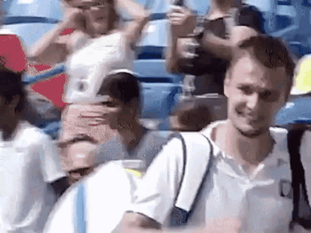 a man with a backpack is standing in front of a crowd of people in a stadium .