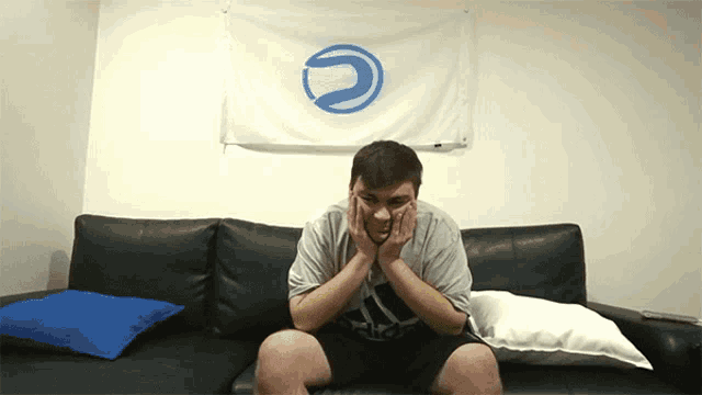 a man sits on a couch with his hands on his face in front of a flag with a blue circle on it